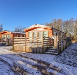 Two wooden cabins with fenced porches surrounded by snow and trees at Pegasus in Felmoor Park