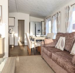 A living area with a brown sofa and dining table with chairs near kitchen and windows at Hercules in Felmoor Park