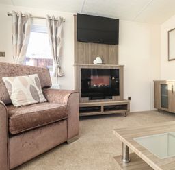 A living room with armchair coffee table TV fireplace sideboard and curtains at Hercules in Felmoor Park