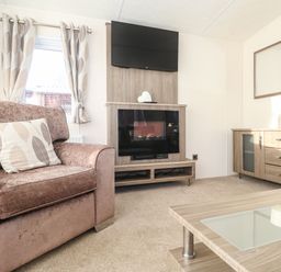 A living room with a pink sofa a fireplace mounted tv wooden cabinet and coffee table at Canis Felmoor Park