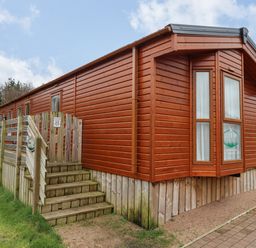 A wooden cabin with a deck and stairs surrounded by grass at Canis in Felmoor Park