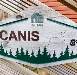 A wooden sign with the text CANIS and an engraving of a house with Est 2020 above trees and a constellation at Felmoor Park
