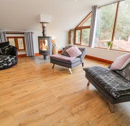 A living room with wooden floor a round patterned sofa two grey chairs with cushions a fireplace and large windows at Monkleigh Mill in Monkleigh near Bideford