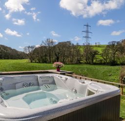 An outdoor hot tub with water surrounded by green fields trees and an electricity pylon at Monkleigh Mill in Monkleigh near Bideford