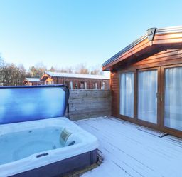 An outdoor deck with a hot tub and wooden buildings in a snowy setting at Draco in Felmoor Park