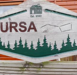 A wooden sign with the text Ursa established 2020 with tree silhouettes and a house image at Felmoor Park