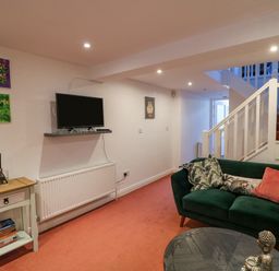 A living room with a green sofa and cushions a small table with books and a diffuser a wall mounted tv and stairs with white railings at 83 Upper John Street in Wexford Town County Wexford