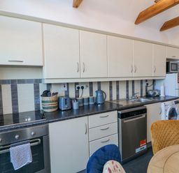A kitchen with white cabinets a black countertop a stainless steel oven dishwasher and washing machine with a round wooden table and colored chairs at 83 Upper John Street in Wexford Town County Wexford