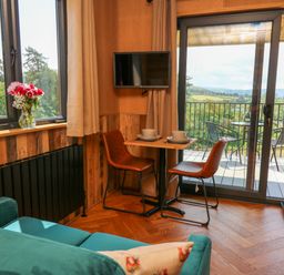 A small dining area with two chairs and a table set with bowls and plates next to a sliding glass door leading to a balcony overlooking green fields and hills at Rooster's Rest in Rhaedr Gwy near Rhayader