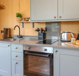 A kitchen countertop with a sink, stovetop, oven, utensils holder, toaster, kettle, and eggs on a cutting board at Rooster's Rest in Rhaedr Gwy near Rhayader