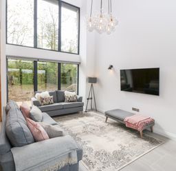 A living room with two grey sofas, a flat screen TV, a floor lamp, a rug, and large windows at Pen-Y-Bryn in Llanfairpwllgwyngyll
