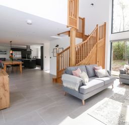 An open living room and kitchen area with gray sofas wooden staircase and dining table at Pen-Y-Bryn in Llanfairpwllgwyngyll