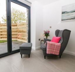 A gray armchair with pink cushion and blanket next to a small side table and sliding glass door at Pen-Y-Bryn in Llanfairpwllgwyngyll