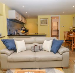 A living room with a beige sofa and kitchen area with blue backsplash at Bradley Stables in Withypool
