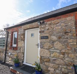 A stone exterior wall with a cream door and two windows at Pips Barn in Brynteg near Benllech