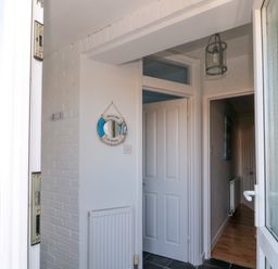 An entrance hallway with white doors a radiator a circular wall mirror and a hanging light at Barnacles in Boulmer near Longhoughton