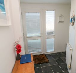 An entryway with a wooden table with a vase and a blue book a door with blinds and a black tiled floor at Barnacles in Boulmer near Longhoughton