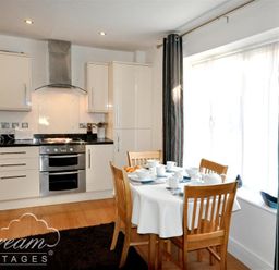 A kitchen with white cabinets a stove and a dining table with chairs set for a meal at Admirals Quarter Apartment 5 in Weymouth
