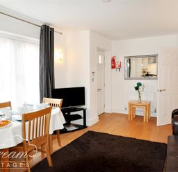 A dining area with a table set for tea next to a living area with a television and brown sofa at Admirals Quarter Apartment 5 in Weymouth