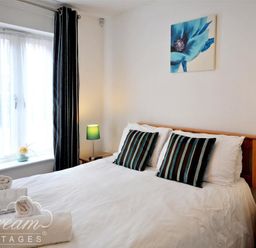 A bedroom with a double bed two striped pillows bedside tables lamps and a window with curtains at Admirals Quarter Apartment 5 in Weymouth