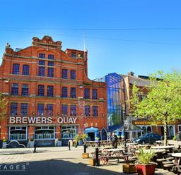 An outdoor seating area with wooden tables and benches in front of a red brick building with Brewers Quay sign at Admiral's Quarter Apartment 5 in Weymouth