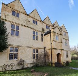 The exterior of a stone building with multiple windows and gabled roofs surrounded by grass and trees at Wick Court Farm in Arlingham near Frampton On Severn