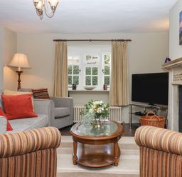 A living room with striped armchairs a glass top wooden coffee table a grey sofa and a TV near a fireplace at Early Mist Cottage in Haytor Vale