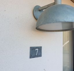 A metal light fixture above a number 7 wall plaque on an exterior wall at 7 Longshore in St Columb Minor