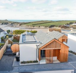A modern house with wooden exterior elements near a beach and grassy hills at 7 Longshore in St Columb Minor