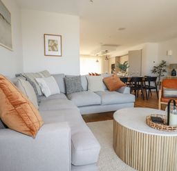A living room with a gray sectional sofa orange pillows and a round wooden coffee table at 7 Longshore in St Columb Minor