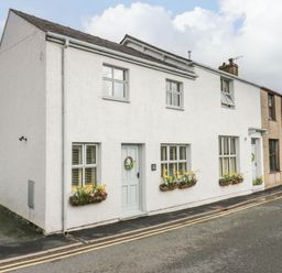 A white two-story house with flower boxes under the windows and gray doors on a curved street at The Anvil in Broughton-In-Furness