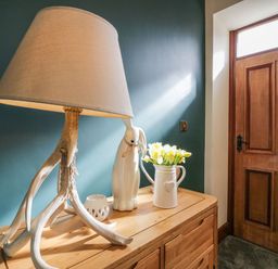 A wooden sideboard with a lamp with antler base vase with flowers and ceramic rabbit figurine near a wooden door at The Anvil in Broughton-In-Furness