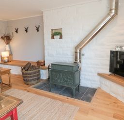 A living room with a wood-burning stove and chimney pipe a basket of firewood a television on a shelf and a sofa at Whiteadder Bank in Berwick-Upon-Tweed
