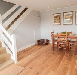 A dining area with wooden table and chairs next to a staircase and a pet bed at Whiteadder Bank in Berwick-Upon-Tweed