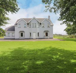 A gray two-story house with multiple windows and a white door surrounded by green lawn and trees at Cloughoge House in Kilrush County Clare