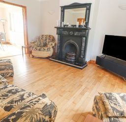 A living room with patterned sofas a black fireplace a television and a wooden floor at Cloughoge House Kilrush County Clare