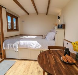 A small room with a bed near an open door a wooden table with croissants flowers and a coffee press at Buzzards in Morchard Bishop
