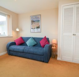 A room with a blue sofa with cushions a lamp a floor lamp a window a framed picture and a white closet at Sky Pocket in Bude