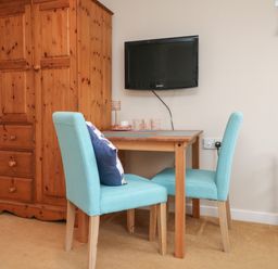 A small dining area with a wooden table and two turquoise chairs near a wooden wardrobe and a wall-mounted TV at Sky Pocket in Bude