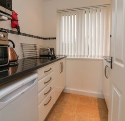 A kitchen with black countertop white cabinets a toaster an oven kettle and a window with vertical blinds at Sky Pocket in Bude