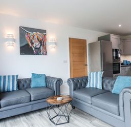 A living room with two grey sofas with blue cushions and a round wooden coffee table at Strawberry Bank - Nuthatch in Pyworthy near Bridgerule