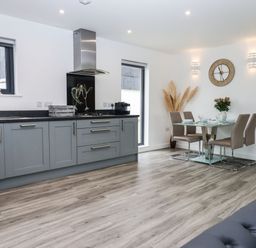 A kitchen and dining area with grey cabinets a glass dining table and beige chairs at Strawberry Bank - Nuthatch in Pyworthy near Bridgerule