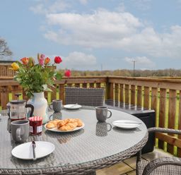 An outdoor patio table set with croissants coffee mugs a vase of flowers and a jar of jam at Strawberry Bank - Nuthatch in Pyworthy near Bridgerule