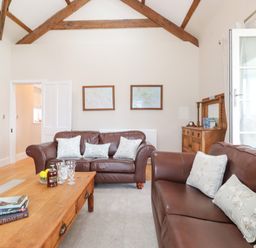 A living room with brown leather sofas and wooden coffee table under wooden ceiling beams at Farnelea West Fleetham near Seahouses
