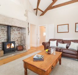 A living room with a stone fireplace a wood stove a brown leather sofa a wooden coffee table and framed maps on the wall at Farnelea West Fleetham near Seahouses