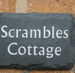 A dark stone plaque with Scrambles Cottage written on it mounted on a stone wall at Scrambles Cottage in Stoke-Sub-Hamdon Somerset