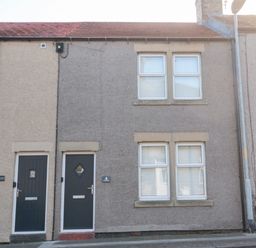 A grey two-storey terraced house with two black doors and four windows at 4 Percy Street in Amble