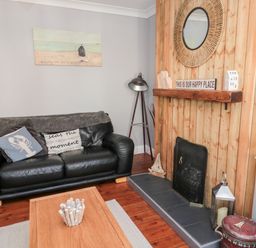 A living room with a black leather sofa cushions wooden coffee table and a fireplace with wooden paneling at 4 Percy Street in Amble