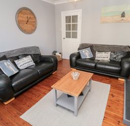 A living room with two black leather sofas a wooden coffee table on a rug and a large clock on the wall at 4 Percy Street in Amble