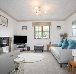 A living room with a gray sofa with blue pillows a television on a stand and a window with striped blinds at Cae Ffynnon in Star near Gaerwen